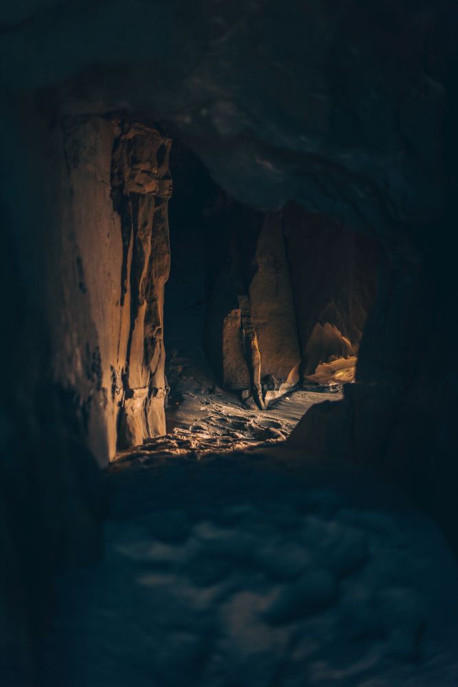The mouth of a cave with dim light shining through. The floor is sand.
